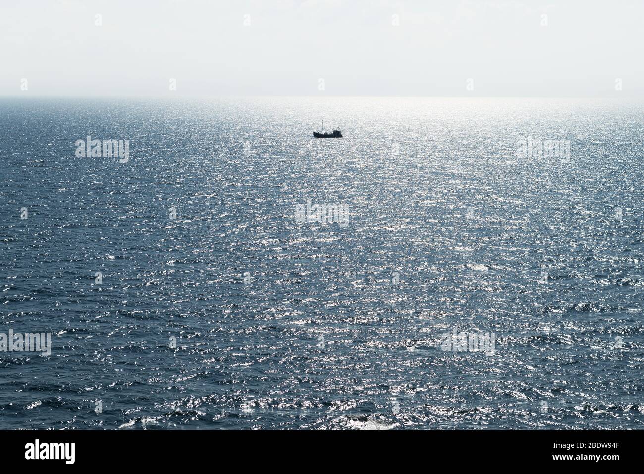 Lonely fishing ship trawler boat on ocean water. Calm clear sea sunny weather. Beautiful horizon of seascape Stock Photo