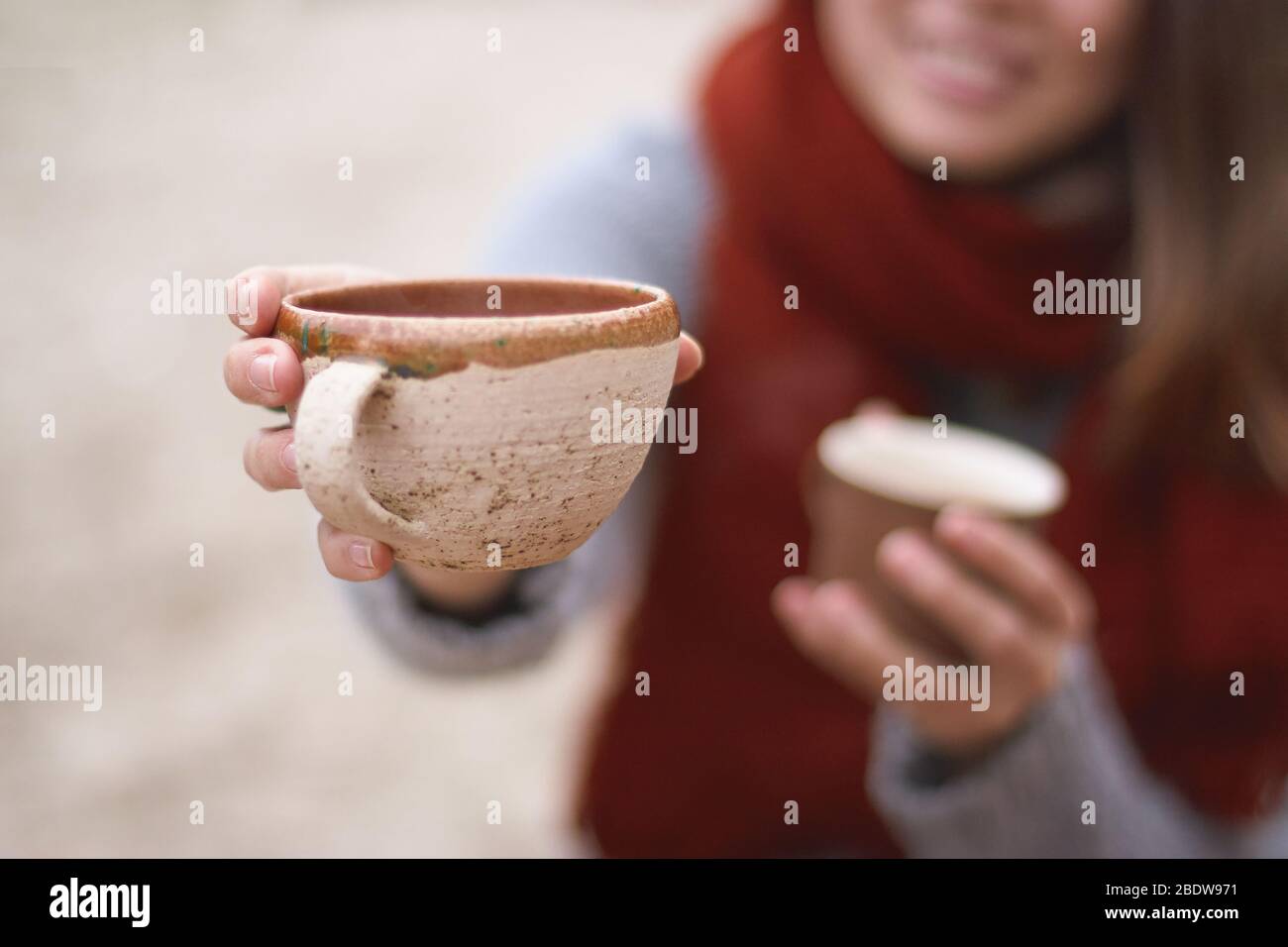 smiling girl holds two cups, one of which she hold out into the frame,  autumn atmosphere Stock Photo - Alamy