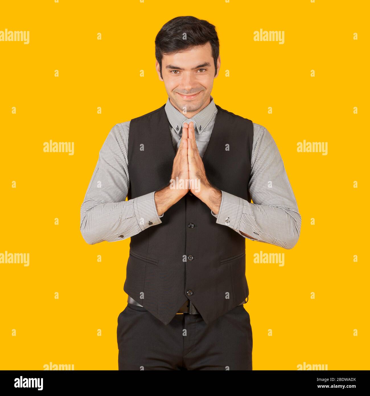 Young businessman in a gray shirt and black vest press the hands together at the chest in sign of respect, smiling and bowing a little. Concept of bus Stock Photo