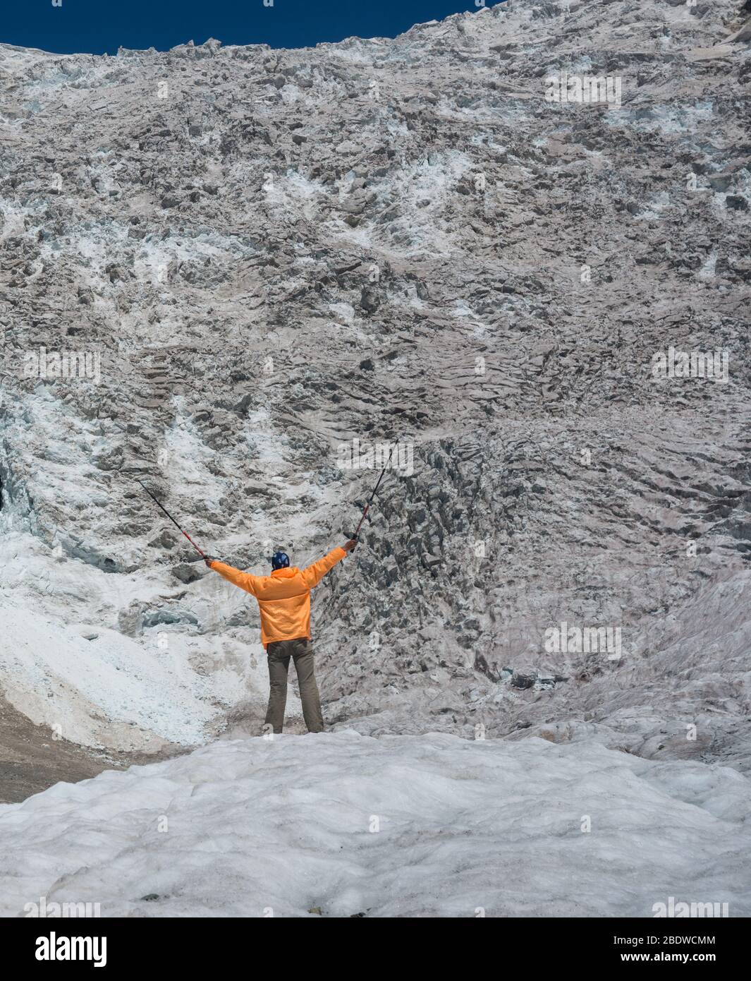 Tourist dressed in orange windbreaker looks at Adishi glacier ( Lardaad). The drop of this icefall is more than 1000 m. Stock Photo