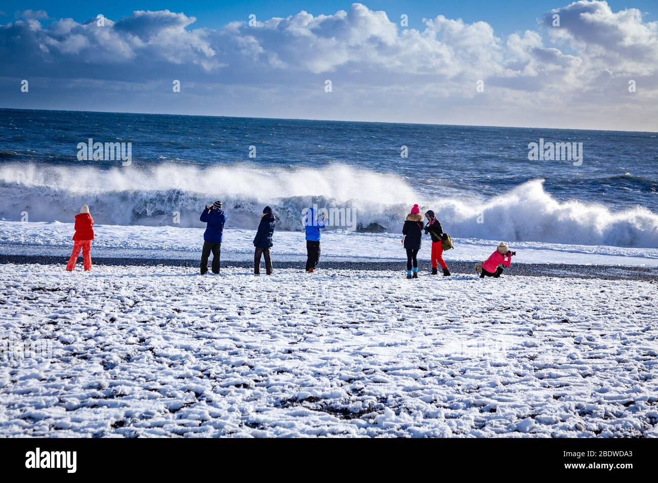 Tourists in winter clothes take photos of sneaker waves breaking on  Reynisfjara black sand beach covered in snow near Vík í Mýrdal in Iceland  Stock Photo - Alamy