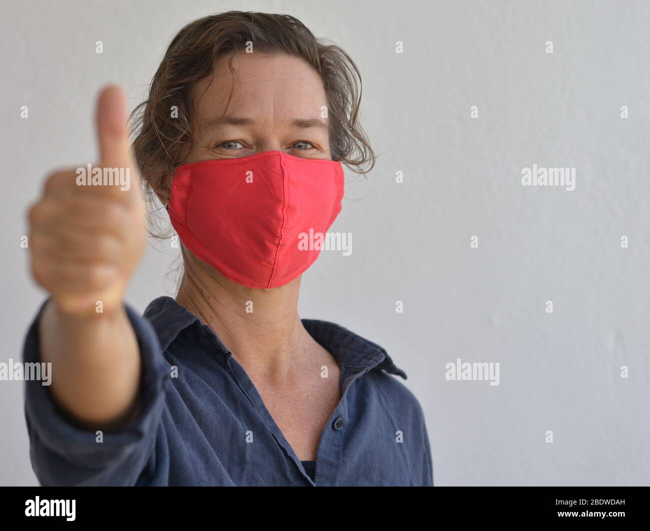 Caucasian woman wears a home-made DIY face mask and gives the thumbs-up sign during the 2019-20 corona-virus pandemic. Stock Photo