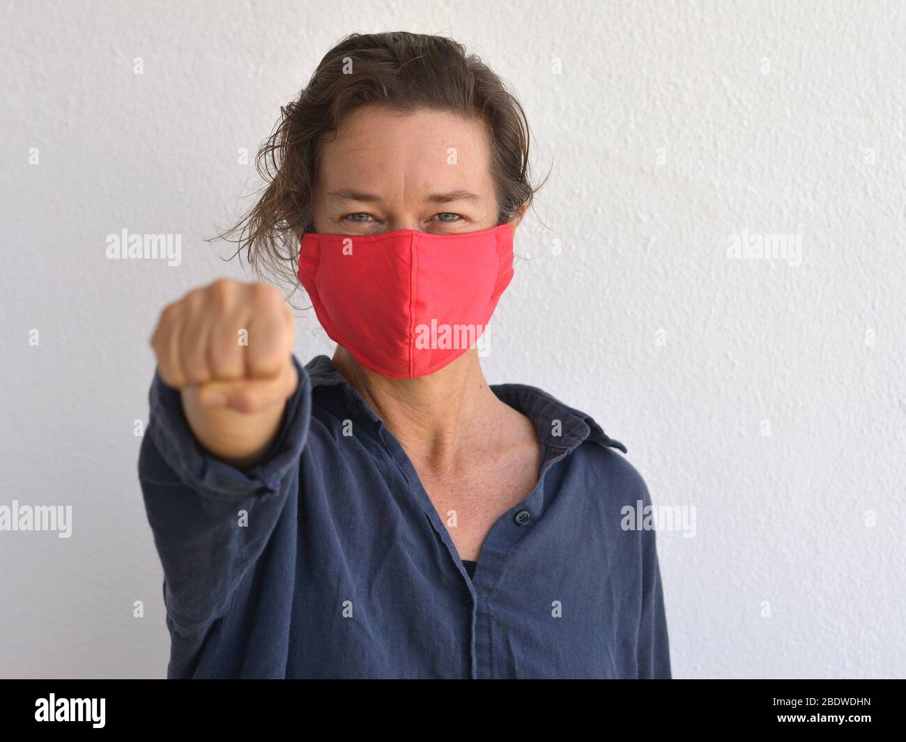 Caucasian woman wears a home-made DIY face mask and shows her fist towards the camera during the 2019-20 corona-virus pandemic - fight Corona. Stock Photo