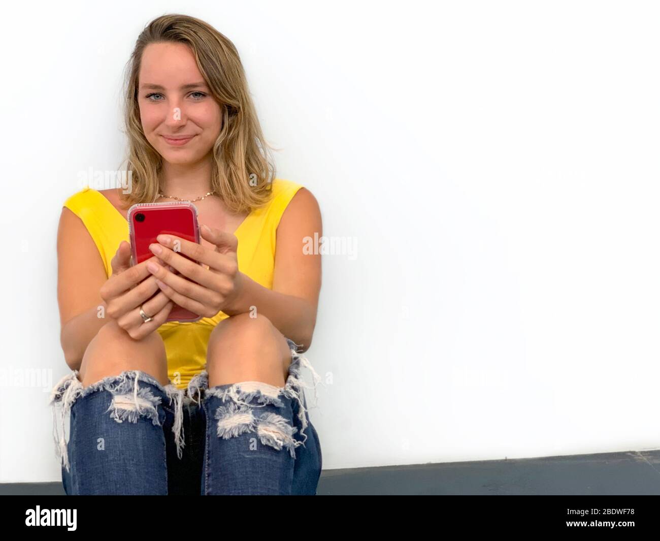 Portrait of young woman sitting on the floor with cell phone Stock Photo