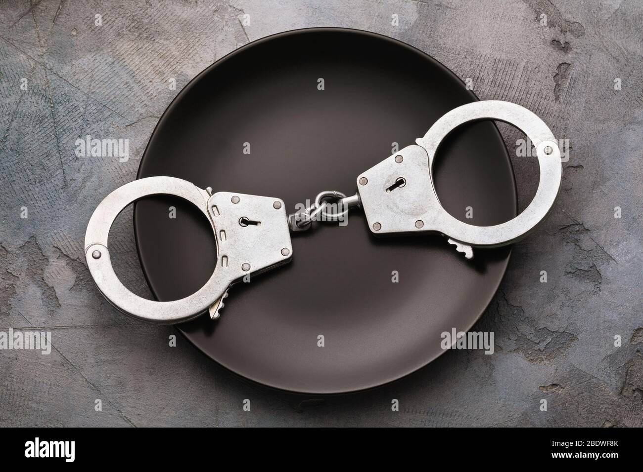 Handcuffs in a black plate, top view. Food Poison Punishment Concept Stock Photo