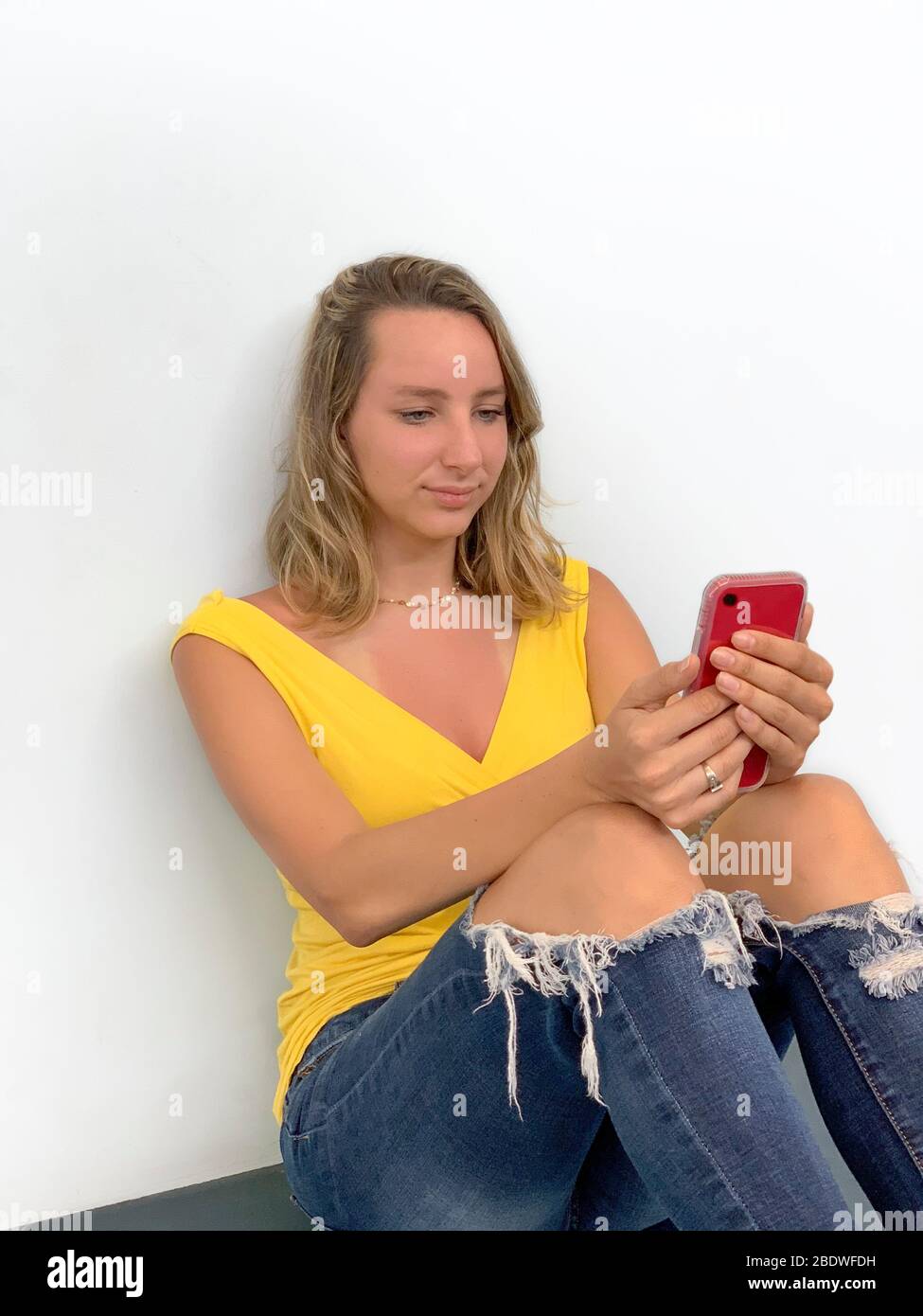 Portrait of young woman sitting on the floor with cell phone Stock Photo