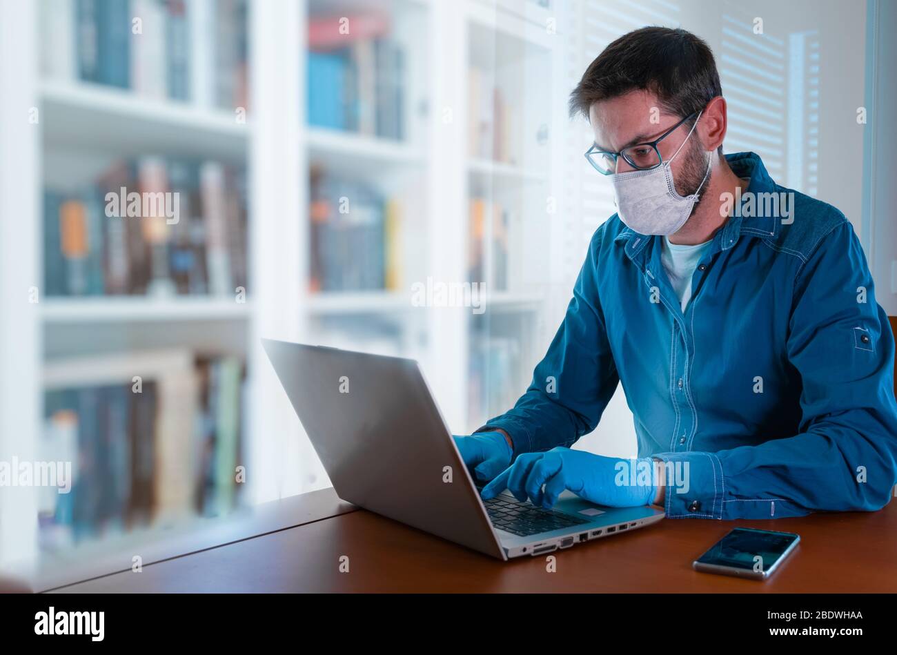 Man with face mask and blue gloves working from home and worried about covid-19 coronavirus Stock Photo