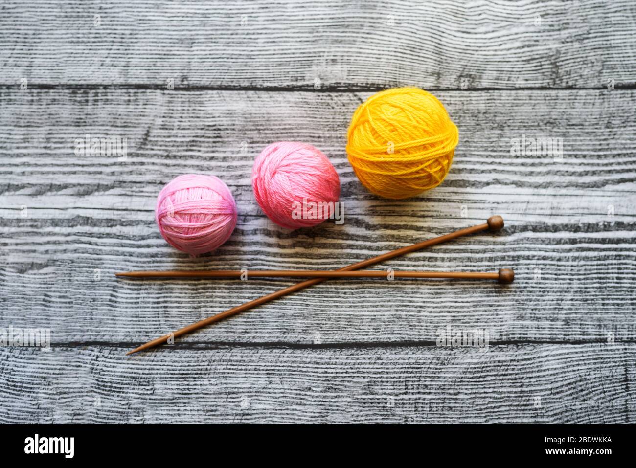 Flat lay of three colored wool balls, knitting needles laying on the wooden background. Stock Photo