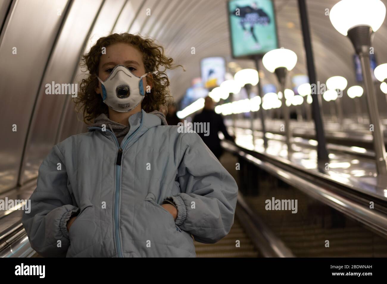 Young teenage girl in a medical mask goes down the subway on an escalator with copy space. Teen in respirator underground Stock Photo