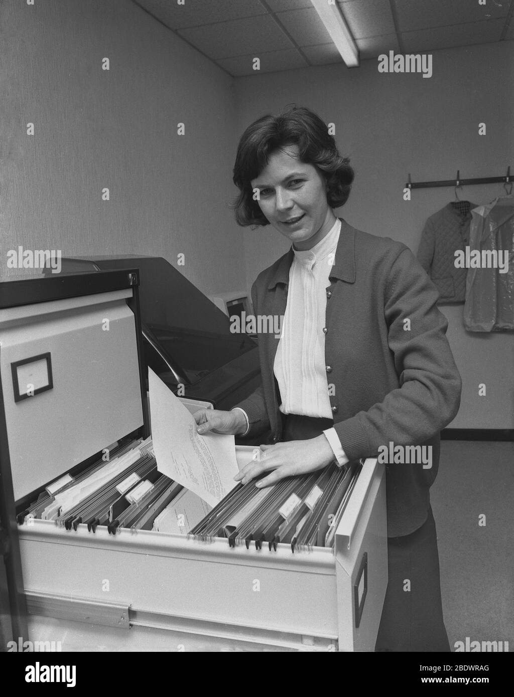 1987, a secretary putting a letter in a draw inside a metal filing cabinet, a storage container used to store copies of correspondence and documents, which can be easily accessed at a later date if needed, England, UK. In this era, paperwork storage equipment such as these were found in most offices and administrative places to keep the workplace both tidy and efficient. Stock Photo