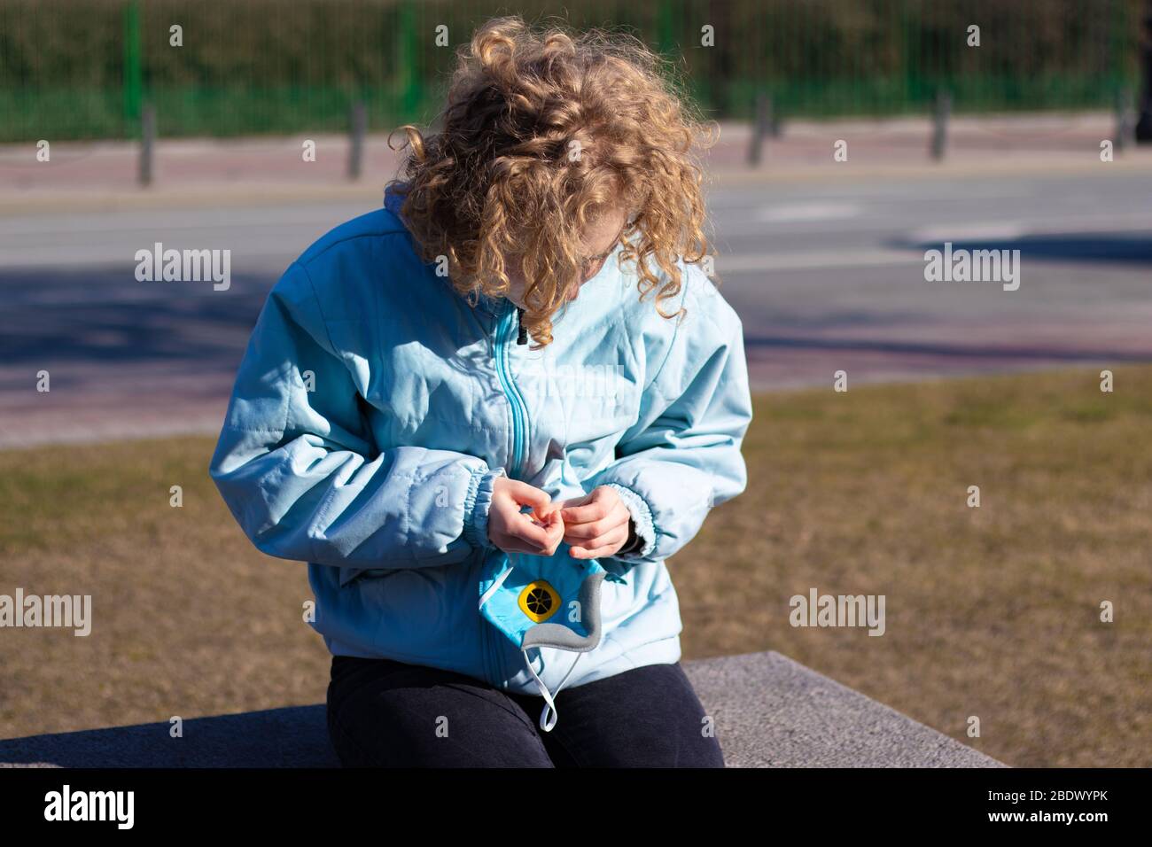 Young girl begins to put on a protective medical respirator on her face. Health protection. Street outdoor photo Stock Photo