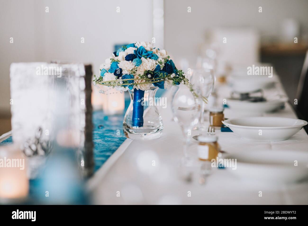 Long dinner tables covered with grey and blue cloth, served with porcelain and blue glasses and rich decorated with flowers stand on the roof of a hou Stock Photo