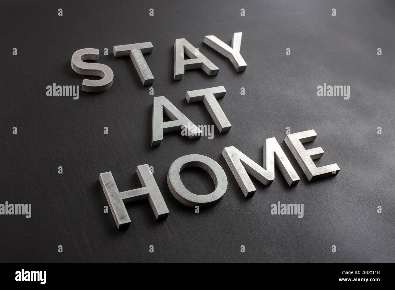 the words stay at home laid with silver metal letters on matte black background in diagonal perspective, slanted full frame view Stock Photo