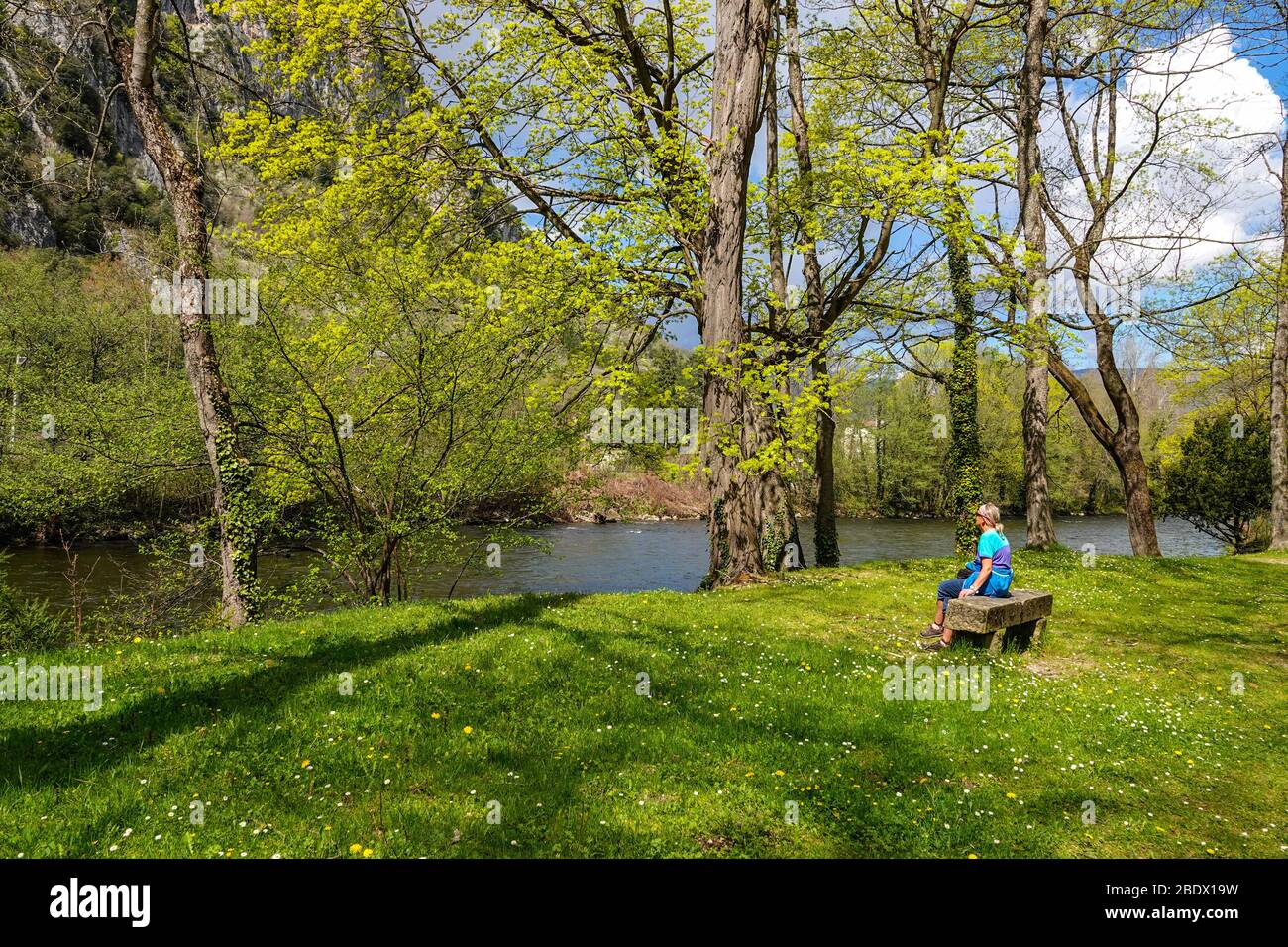 Solitary female sat on stone bench by River Ariege, Ornolac Ussat les Bains, Ariege, French Pyrenees, France Stock Photo