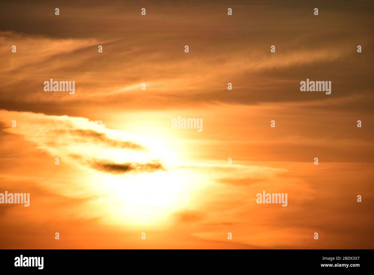 Setting sun set in swath of red and orange hued cloud formations, giving an unearthly appearance. Stock Photo