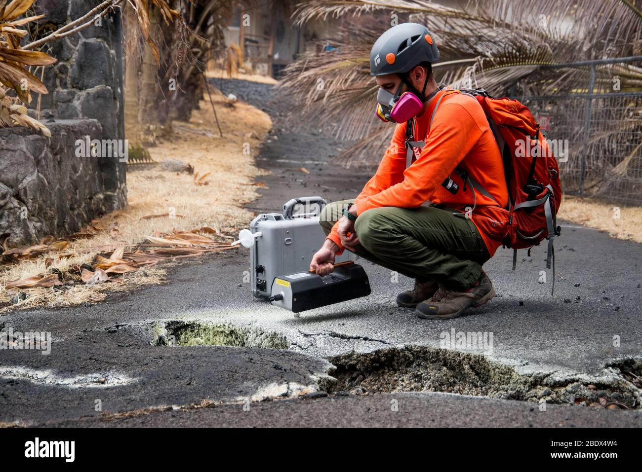 U.S. Geological Survey (USGS) volunteer Allen Lerner uses a sulfur dioxide (SO2) sensor to test the air quality after the Kīlauea volcanic eruption on May 19, 2018. Note the yellow sulfur deposits on the asphalt around the crack in the street.  The residential area of Leilani Estates has been evacuated due to the high concentration of SO2 emitting from the cracks in the earth that spilled lava into the subdivisions. Stock Photo