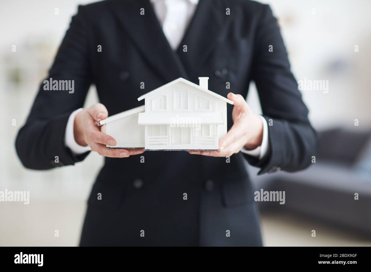 Close-up of real estate agent in black suit holding model of the house ...