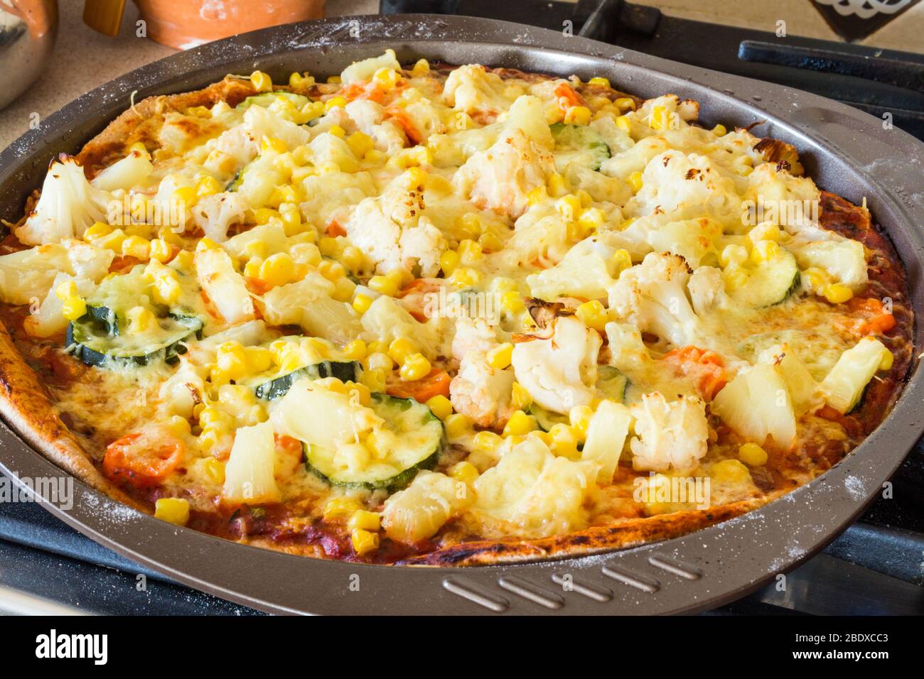 Homemade vegetarian veggie pizza with cheese, pineapple, corn, vegetables, zucchini, cauliflower in baking tray tin Stock Photo