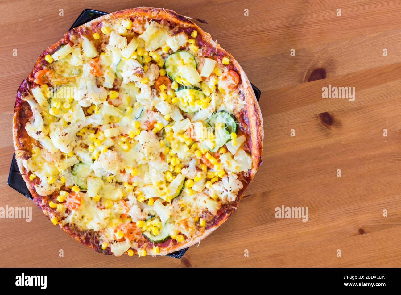 Homemade vegetarian veggie pizza with cheese, pineapple, corn, vegetables, zucchini, cauliflower on wooden table Stock Photo