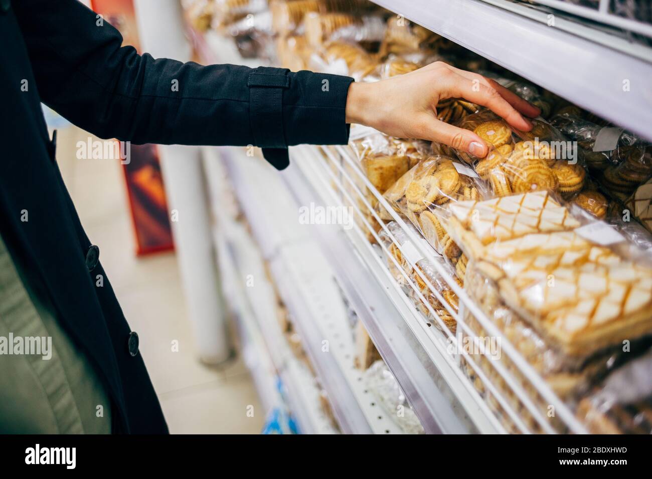 Young woman choosing cookies near shelf in bakery department of grocery