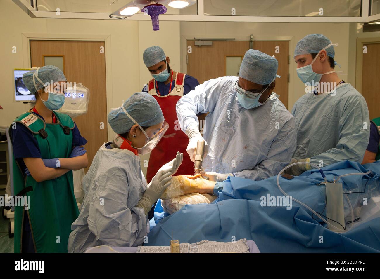 Surgeons and technicians insert a metal plate into the ankle area of a patient's foot to repair a fractured bone and damaged joint. Stock Photo