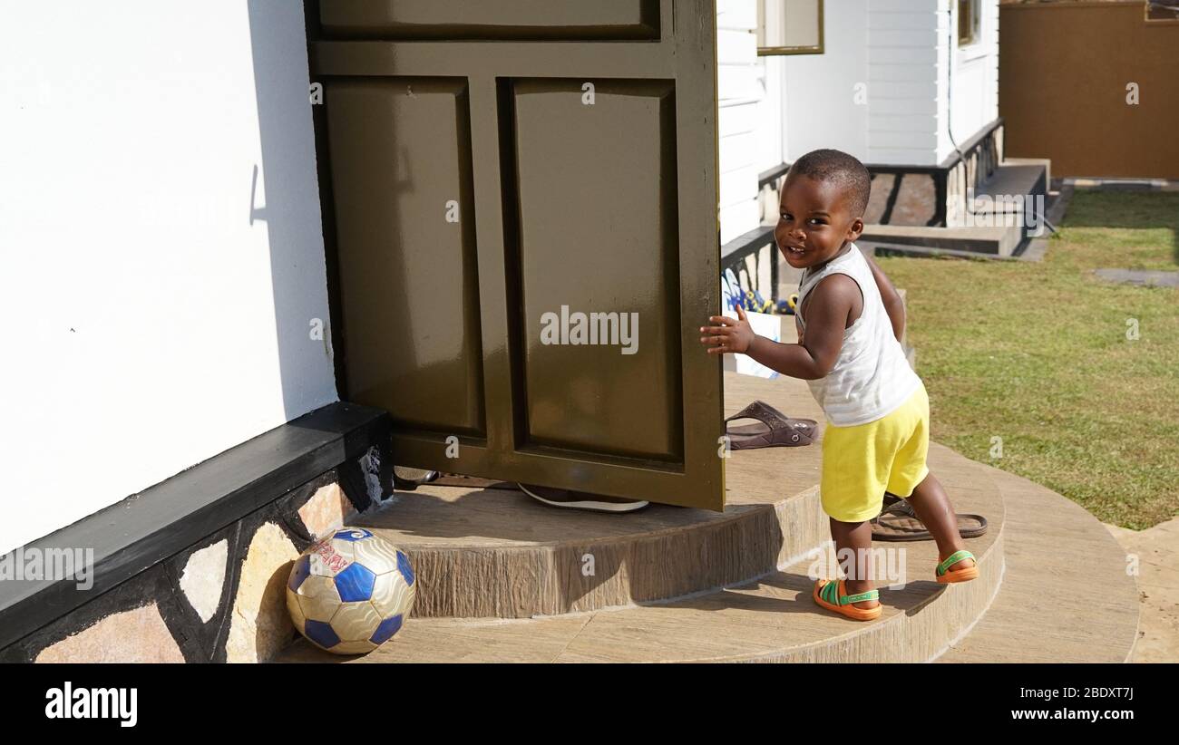 A little happy and smiling African-American boy is running in the house after playing football at home's garden Stock Photo