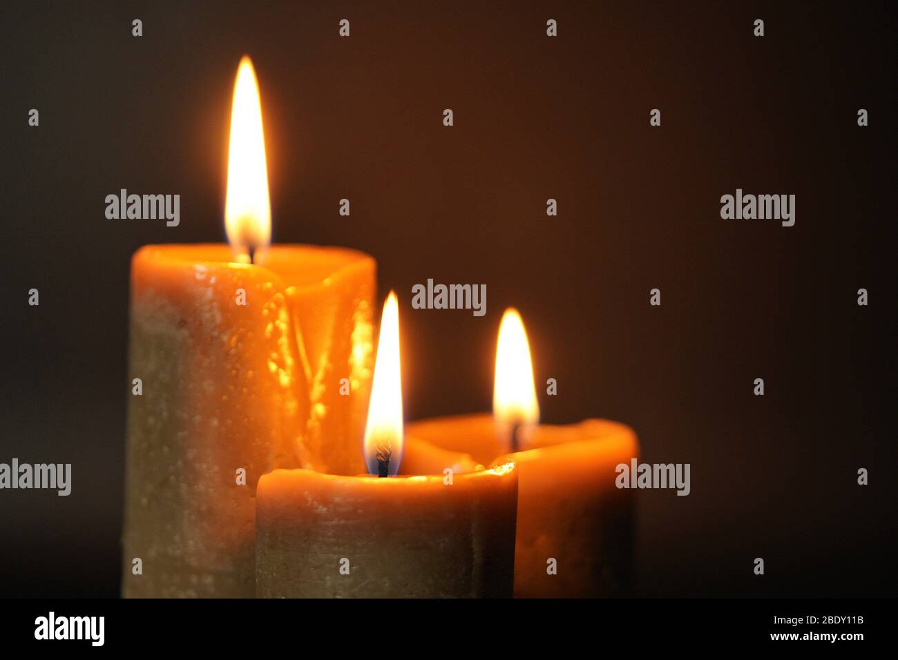 Group of three brown burning candles on a black background close-up. Concept of comfort,romance,mystic,occultism,religion,a symbol of memory.Copy Stock Photo