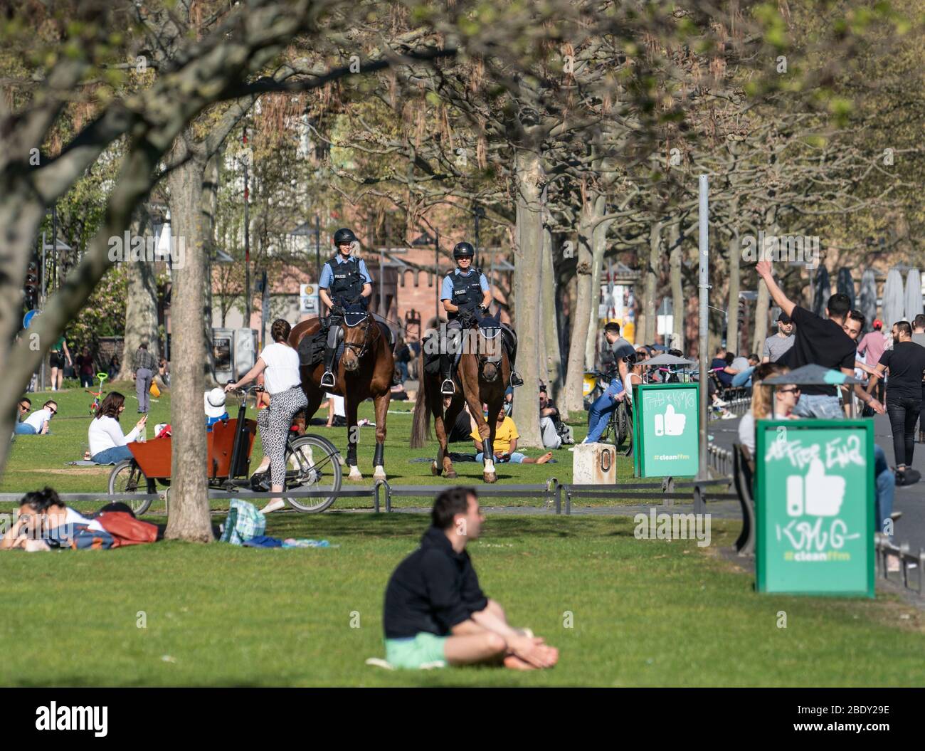 10 April 2020, Hessen, Frankfurt/Main: Two policewomen (M) ride on their horses over the meadows populated by people along the northern bank of the Main River and check that the ban on contact, which is still in place because of the corona pandemic, is being observed. Photo: Frank Rumpenhorst/dpa Stock Photo
