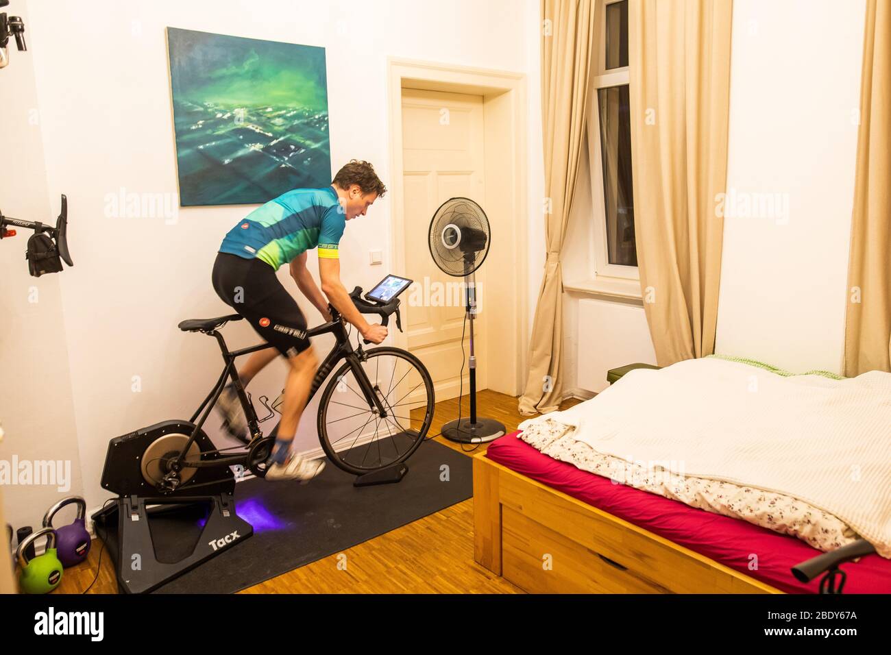 03 April 2020, Lower Saxony, Hanover: Amateur cyclist Nico Herzog trains on  the roller trainer or exercise bike in his bedroom. He uses a bike  simulation app called Zwift in winter and