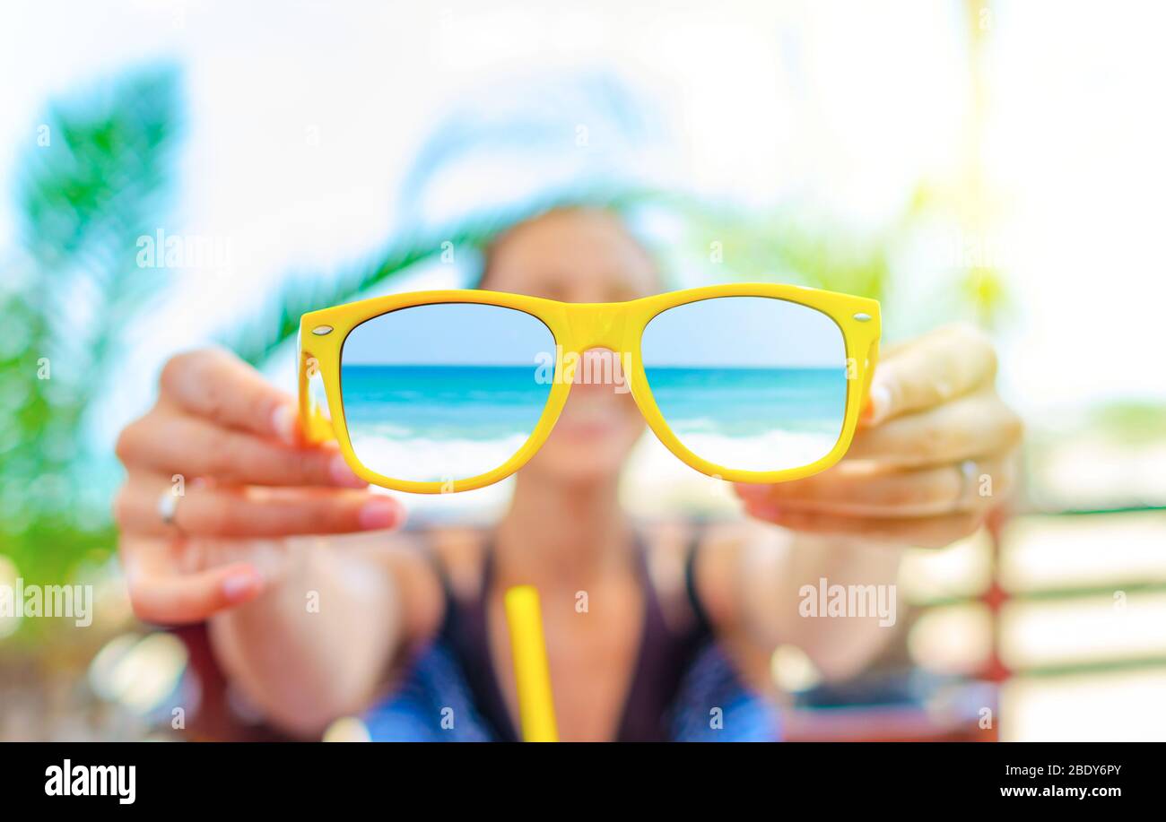 Young woman is holding sunglasses in her hand against the background of palms. Stock Photo