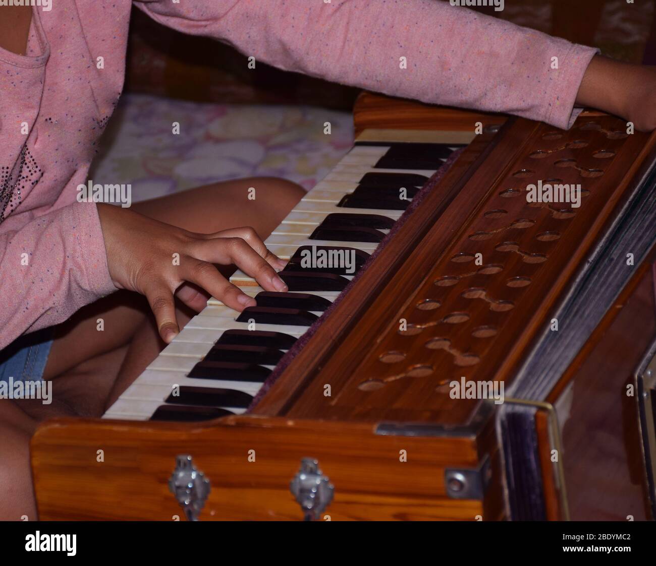 Close shot of Indian girl child playing harmonium reeds or keyboard Stock Photo