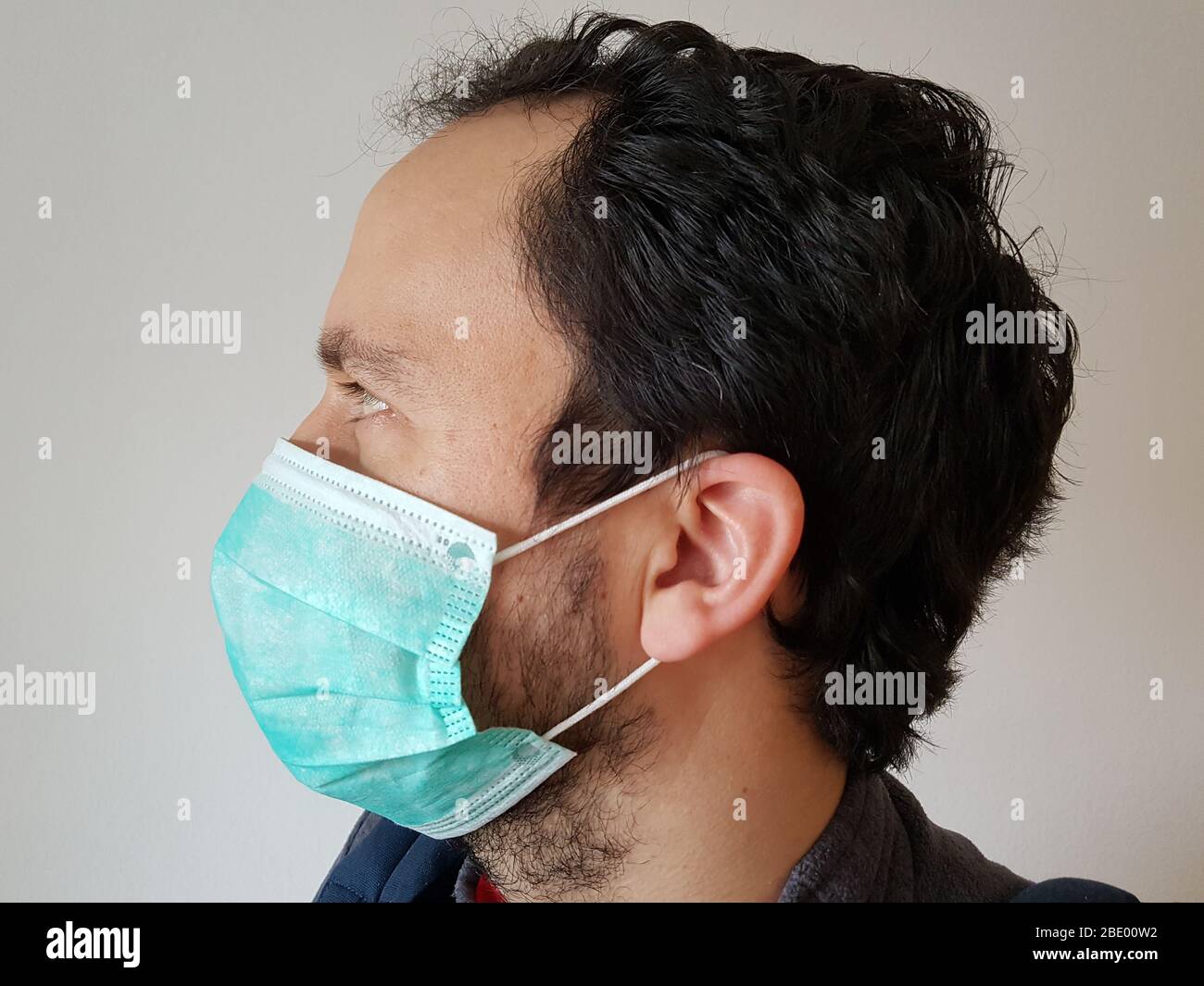 Side view of one person ( man / male ) wearing a green surgical mask or face mask ( mouth / nose ) for infection protection e.g. corona virus covid-19 Stock Photo