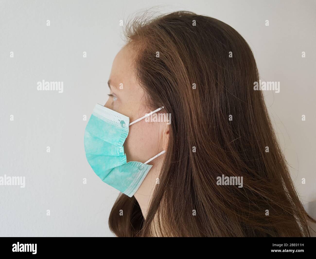 One person ( woman / female ) side view wearing green surgical mask or face mask ( mouth / nose ) for infection protection e.g. corona virus covid-19 Stock Photo