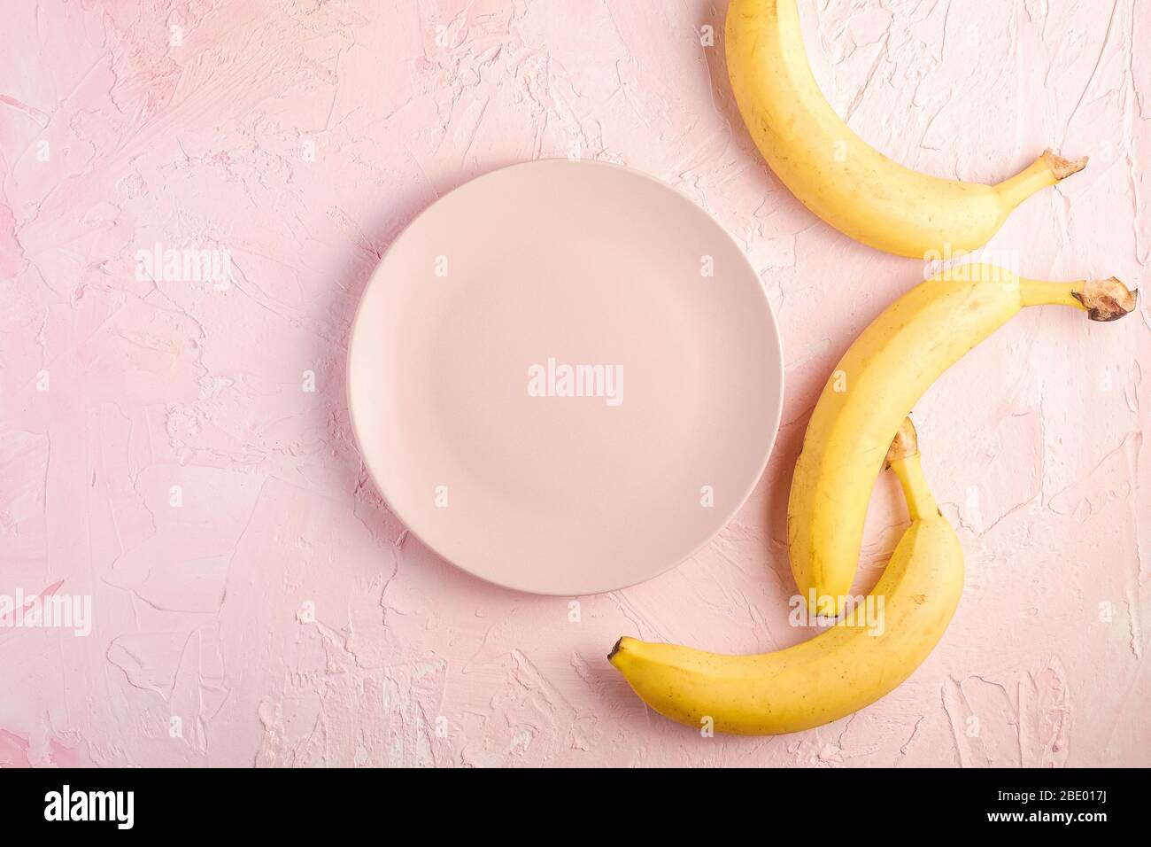 Banana fruits with empty pink plate on pink textured background, top view copy space Stock Photo