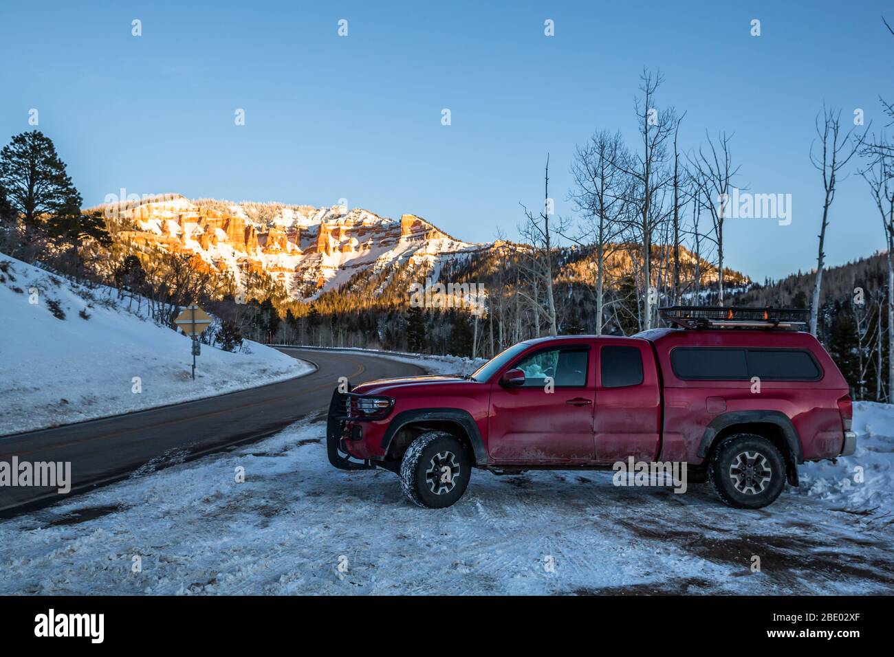 Red pickup covered in salt from the highway snow melting operations. Parked along the road toward red cliffs at sunset. Stock Photo