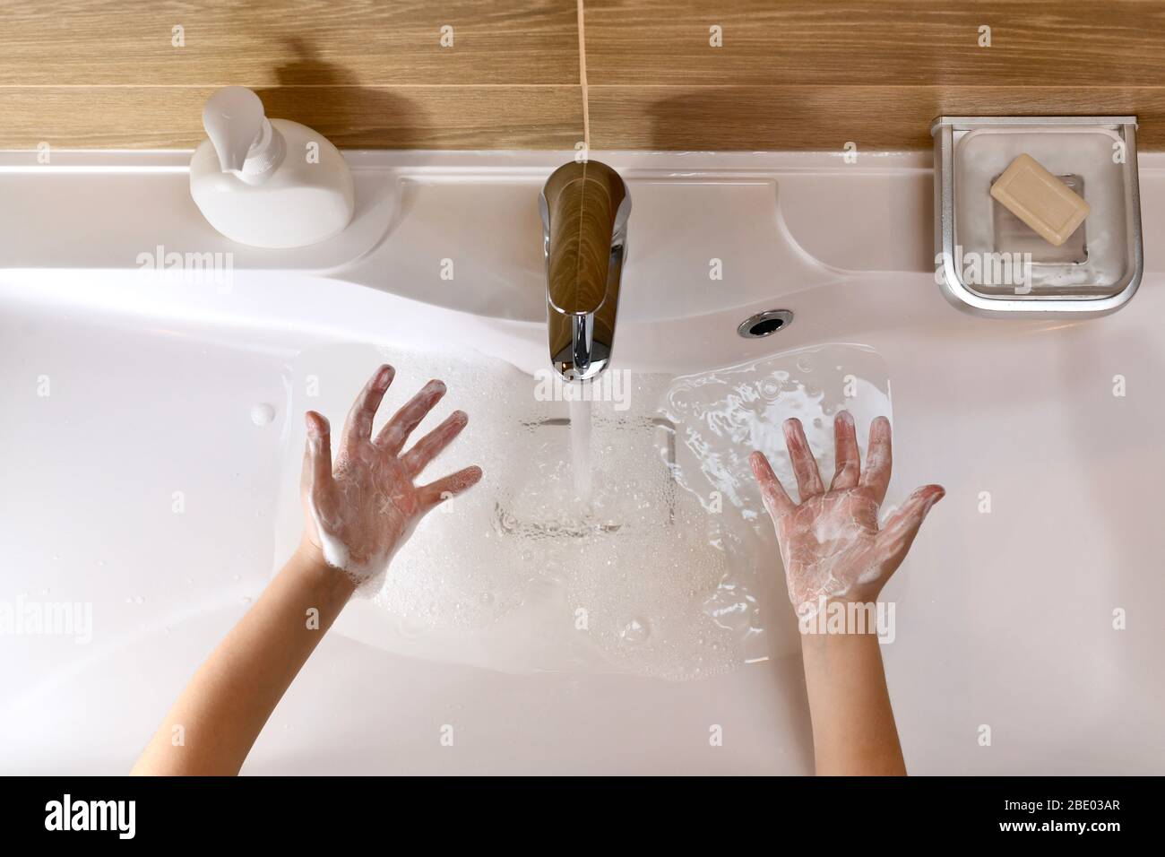 The child shows the palms rolled up the soapy foam-filled hands, above the sink with pouring water. Stock Photo