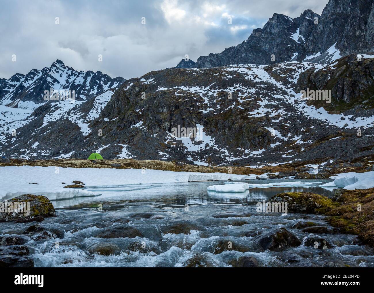 Camping overa frozen lake and waterfall below massive rocky peaks in the remote Alaskan wilderness of the Talkeetna Mountains. Stock Photo