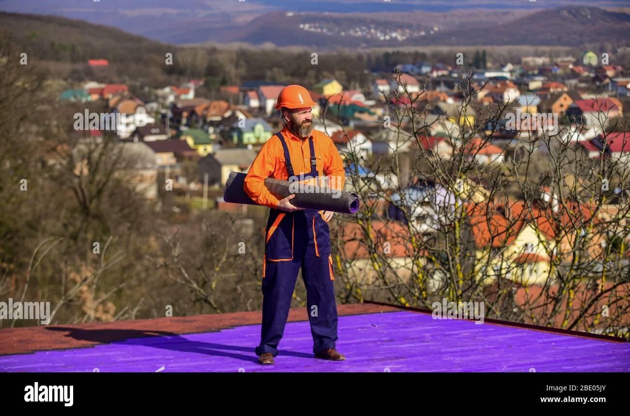 Building house. Apply plastic coatings membranes fiberglass or felt over sloped roofs before applying shingles. Roofer repair roof. Roof installation. Man hard hat work outdoor landscape background. Stock Photo