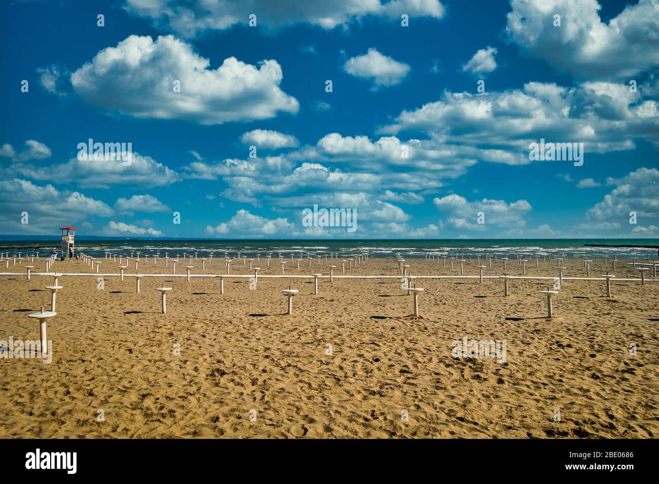 Empty beach of Grado, Italy with lots of Parasol stands and blue sky. Few white clouds, orange sand. Springtime day shot, copyspace Stock Photo