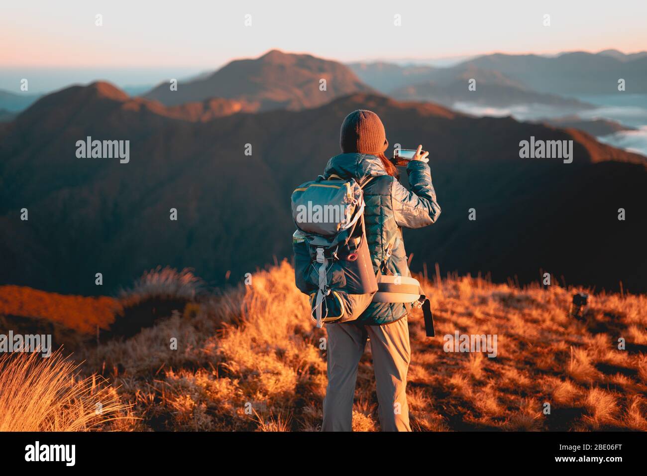 Adult female taking  photo using her mobile phone at sunrise at Mount Pulag National Park, Benguet, Philippines. Stock Photo