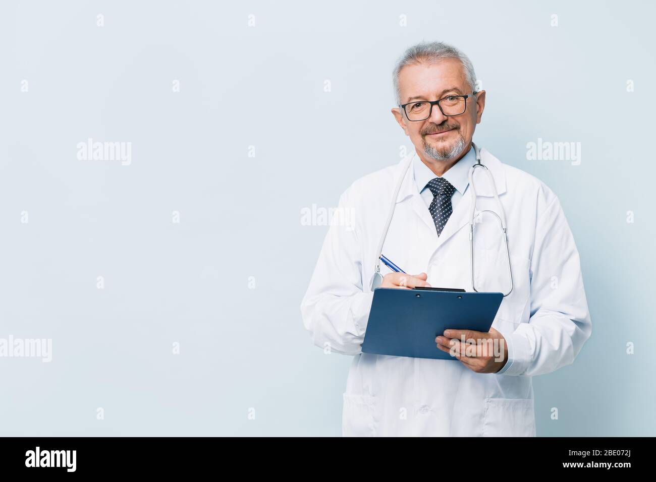 Elderly bearded male doctor in white uniform with a stethoscope with a blue folder. Doctor on the background of a medical research laboratory. Stock Photo