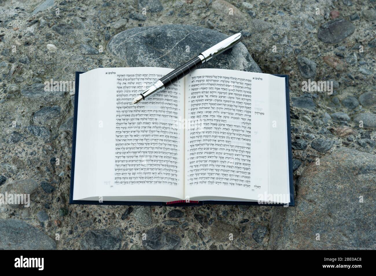 Open Hebrew Bible - TANAKH (Torah, Neviim, Ketuvim - The Law, The Prophets, The Writings) with fountain pen outdoors. Isolated on stones background. Stock Photo