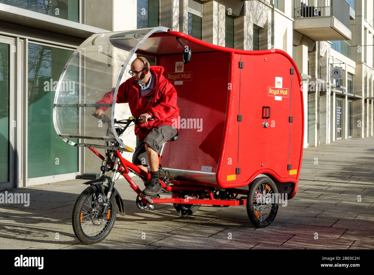 Cycling Royal Mail postman on electric cargo bike, e-Trike, powered by a combination of solar, battery, pedal and brake technology Stratford London UK Stock Photo