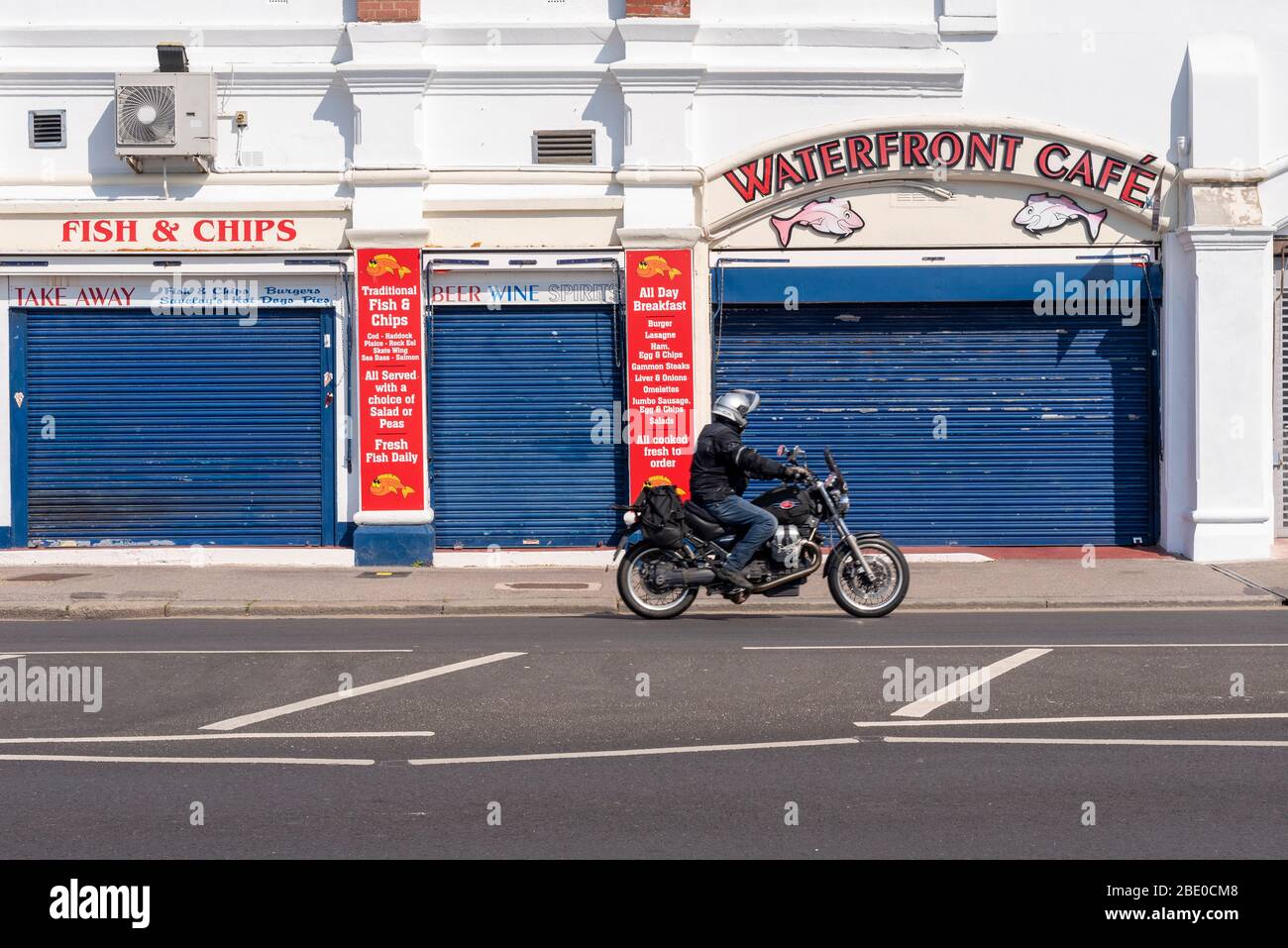 Motorcycle rider passing shut cafe sunny day on Southend seafront on Easter Bank Holiday during COVID-19 Coronavirus pandemic lockdown period Stock Photo