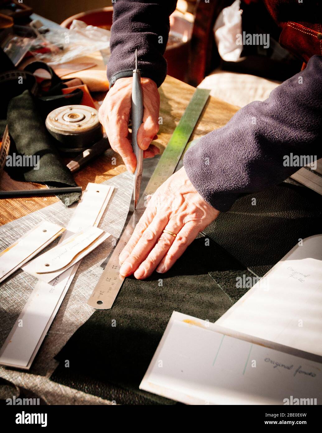 leather  craftsman cutting a piece of leather with a knife Stock Photo