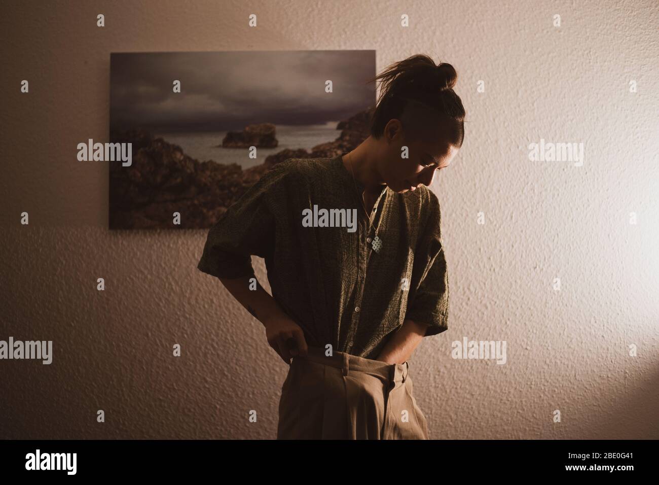 androgynous woman tucks shirt in front of artwork in home at night Stock Photo