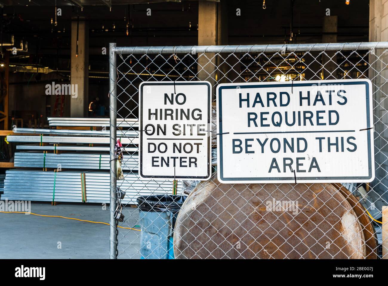 Signs at the entrance to a construction site stating that there is no hiring on site and hard hats are required beyond this area and cautioning people Stock Photo