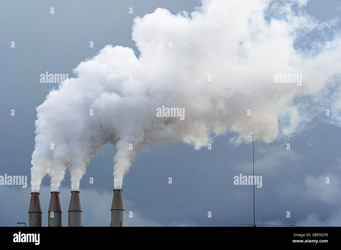 Smoke and steam rising into the air from power plant stacks; dark clouds background; concept for environmental pollution and climate change Stock Photo