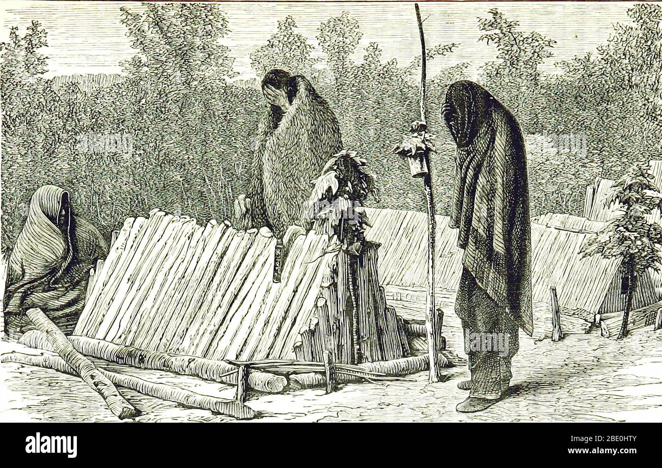 Chippewa or Ojibwe graves and mourners, in a feast for the dead, 1873. 'In front of the nearest grave is seen the grave post, with leaves and a vessel for offerings tied to it. In the end of the wooden structure covering the grave is a hole for inserting offerings of food, and at top it is ornamented with leaves. At the side is hung the worked knife-case of the deceased, and above is a headdress of feathers.' John William Dawson. The Ojibwe (also Ojibwa), or Chippewa are one of the largest groups of Native Americans and First Nations on the North American continent. Stock Photo