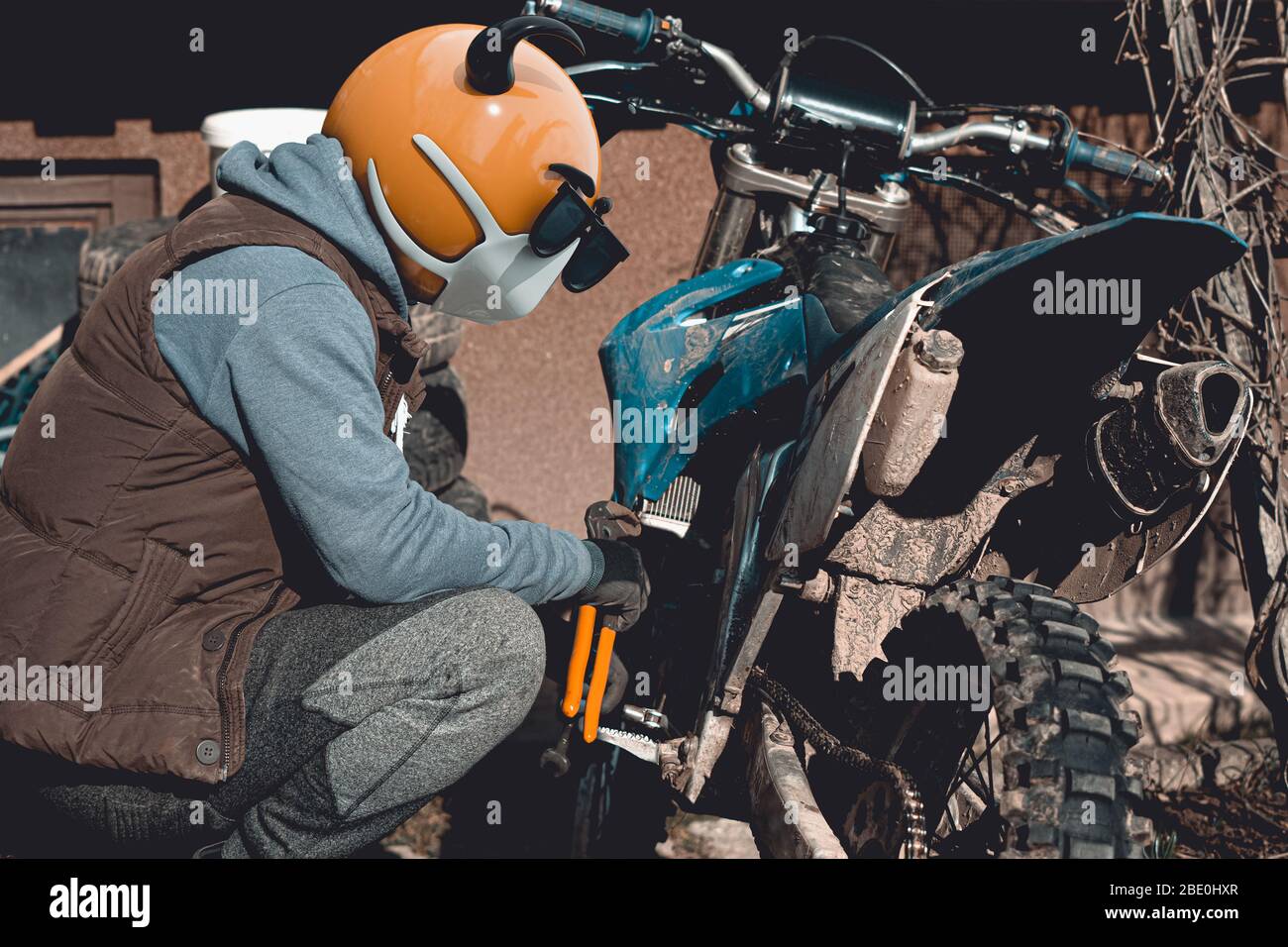 Emoji motocross rider with fancy nerd sunglasses, preparing his motorcycle for a race before season. Emoji with mask protecting against coronavirus Stock Photo